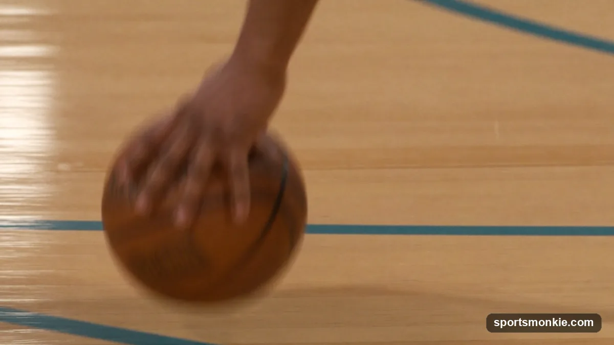 A close-up of a player's hand controlling a low basketball dribble on a hardwood court