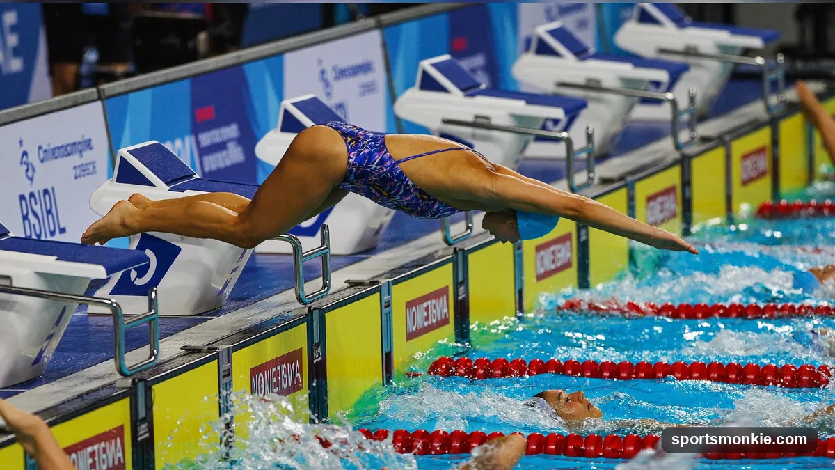 Four swimmers on starting blocks preparing for a medley relay exchange in a competition pool