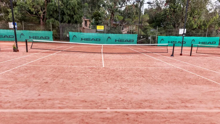 File photo from 21 January 2023: an empty clay tennis court in Melbourne, Australia, photographed looking down the net. It does not show Milicevic or any ITF event. The cropped 16:9 derivative is offered under the same CC BY-SA 4.0 licence as the original.